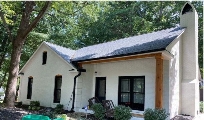 After: the same house finished in white with cedar porch posts, dark window frames and a planted bed along the front.