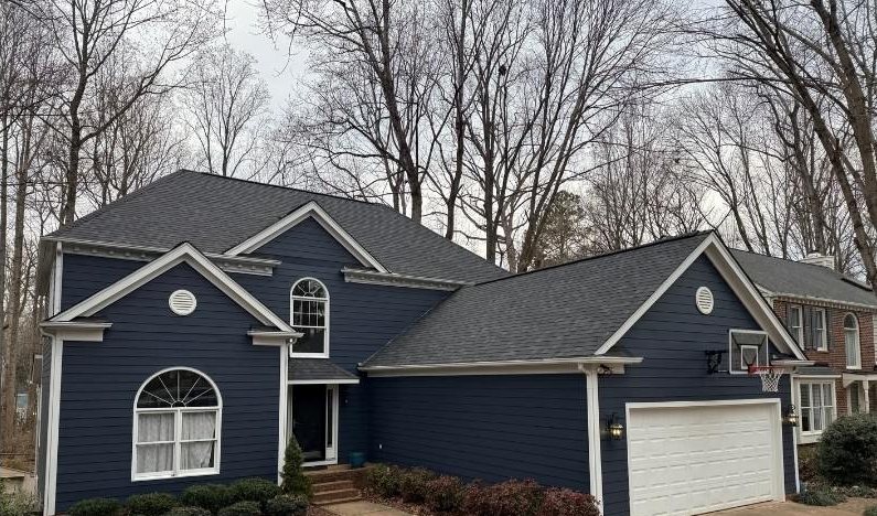 After: the finished dark architectural shingle roof over navy siding, drive cleared.