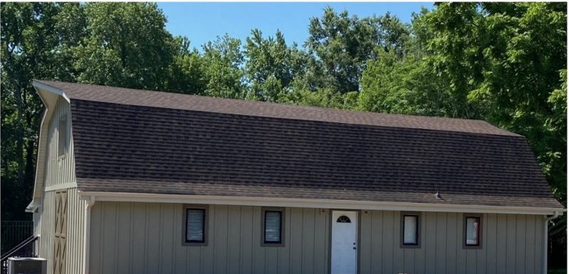 After: the finished clubhouse in dark siding under a new gambrel roof, lot cleared.