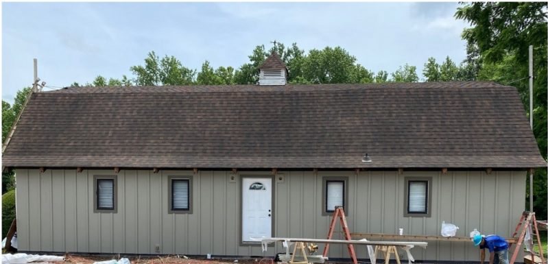 Before: a long single-story clubhouse mid-job, siding materials and trestles across the parking lot.
