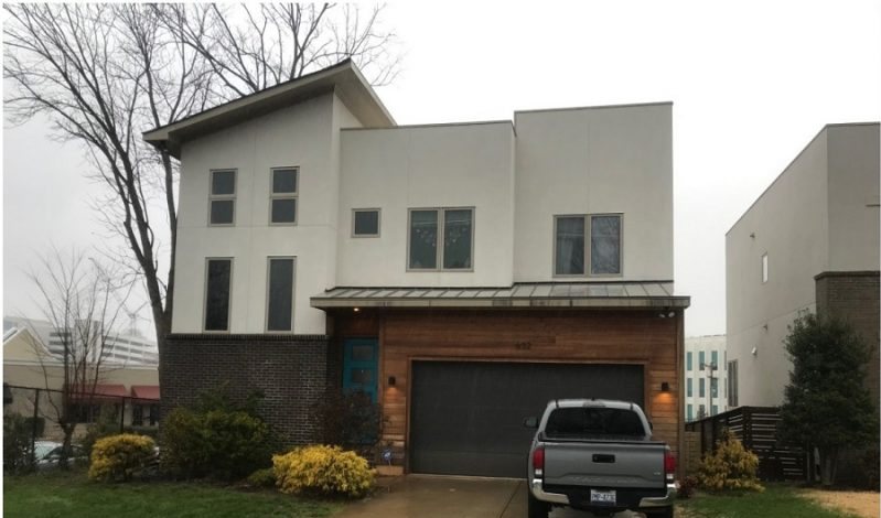 Before: a modern infill house in plain stucco and brick with a dark garage door and a pickup on the drive.