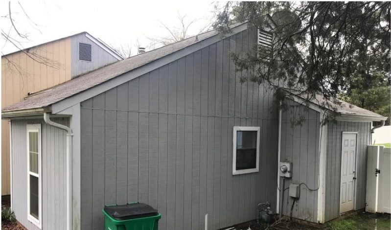 Before: a gray side elevation and garage with a wheelie bin and weathered siding.