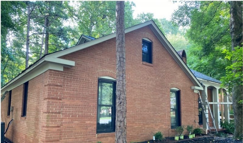 Before: a dark red-brick single-story home with black window frames and a ladder against the gable.
