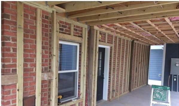 Before: an open porch framed out, bare studs against brick with tools and a ladder on the slab.