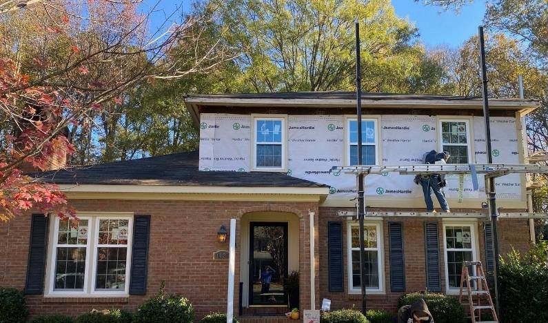During: the front elevation under scaffolding with ladders against the brick and a worker at the door.