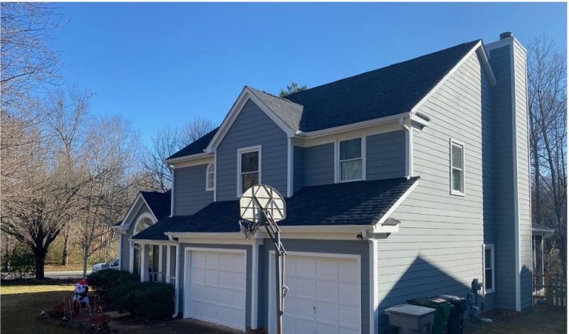 After: the same frontage in blue-gray siding with white garage doors and a cleared drive.