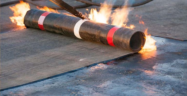A roll of rubber membrane roofing being heat-welded onto a flat roof deck