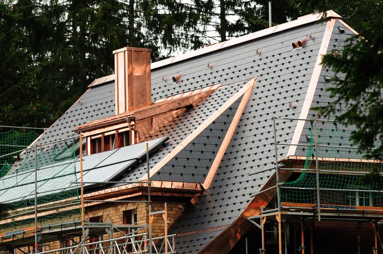 Copper roofing and flashing being installed on a steep shingled roof