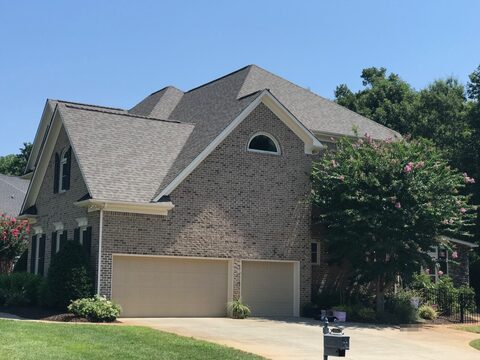 Stucco home with a new gray architectural shingle roof and an arched gable window