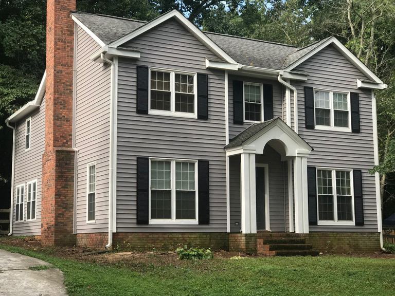 Cream vinyl siding and white trim on a two-story colonial with a brick chimney