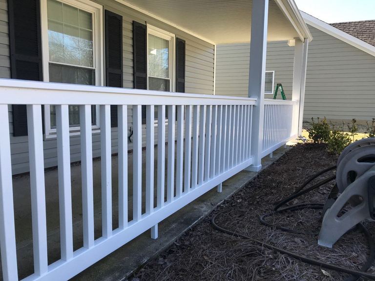 A white vinyl porch railing running the length of a covered porch, with the house's siding and porch ceiling behind it.