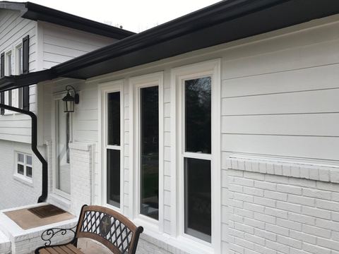 Black-framed windows on a white-sided porch with a bench and a brick base