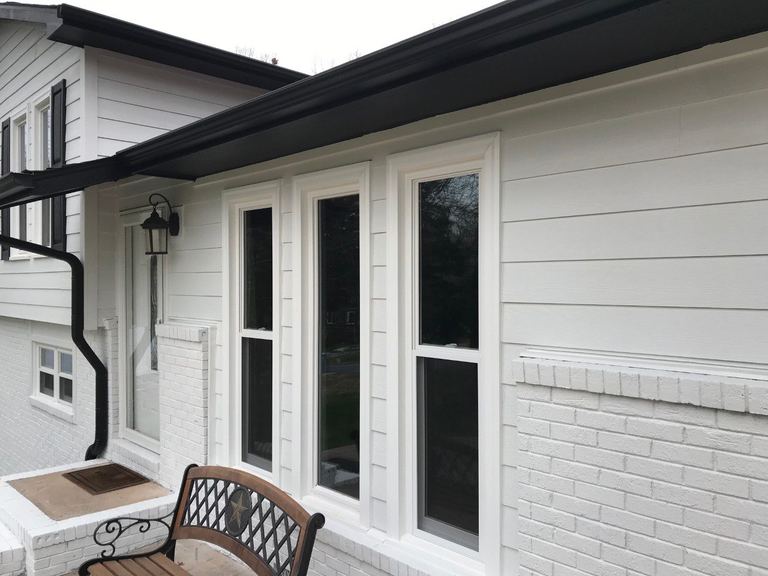Black-framed windows on a white-sided porch with a bench and a brick base