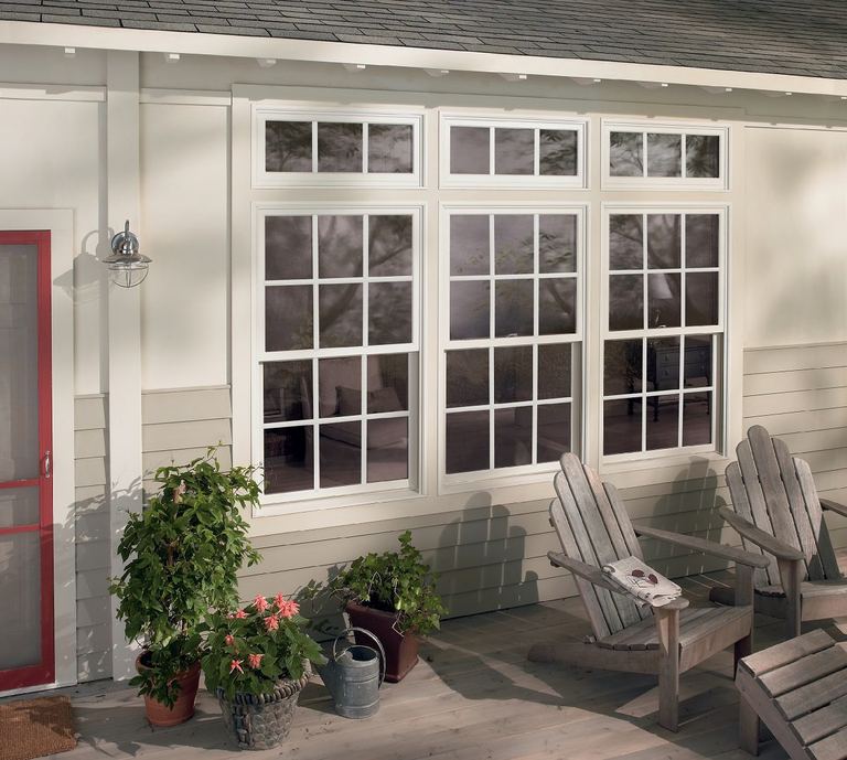 A bank of white windows along a covered porch with wooden chairs