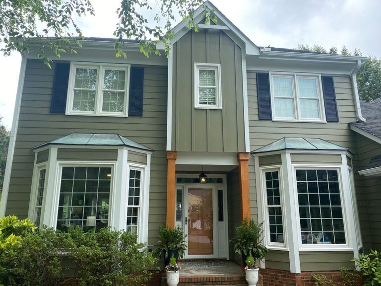 A Huntersville home in sage-green board-and-batten and lap siding with navy shutters, bay windows and a cedar porch post.