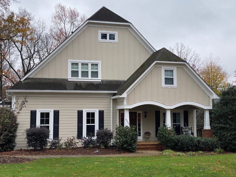Tan fiber cement siding with black shutters on a craftsman-style home