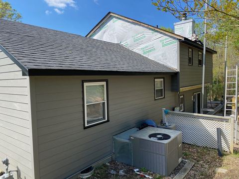 A home partway through siding replacement, with weather barrier still exposed on the upper wall