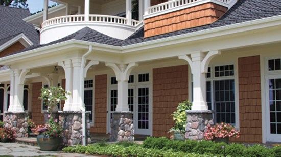 Covered porch with white columns on stone bases against red shake siding