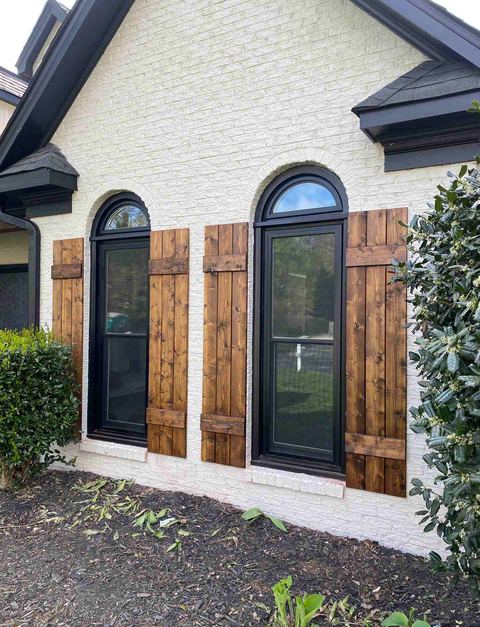 Arched windows with custom stained-wood shutters on a white brick home