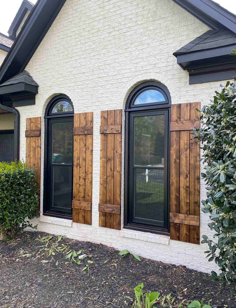 Arched windows with custom stained-wood shutters on a white brick home