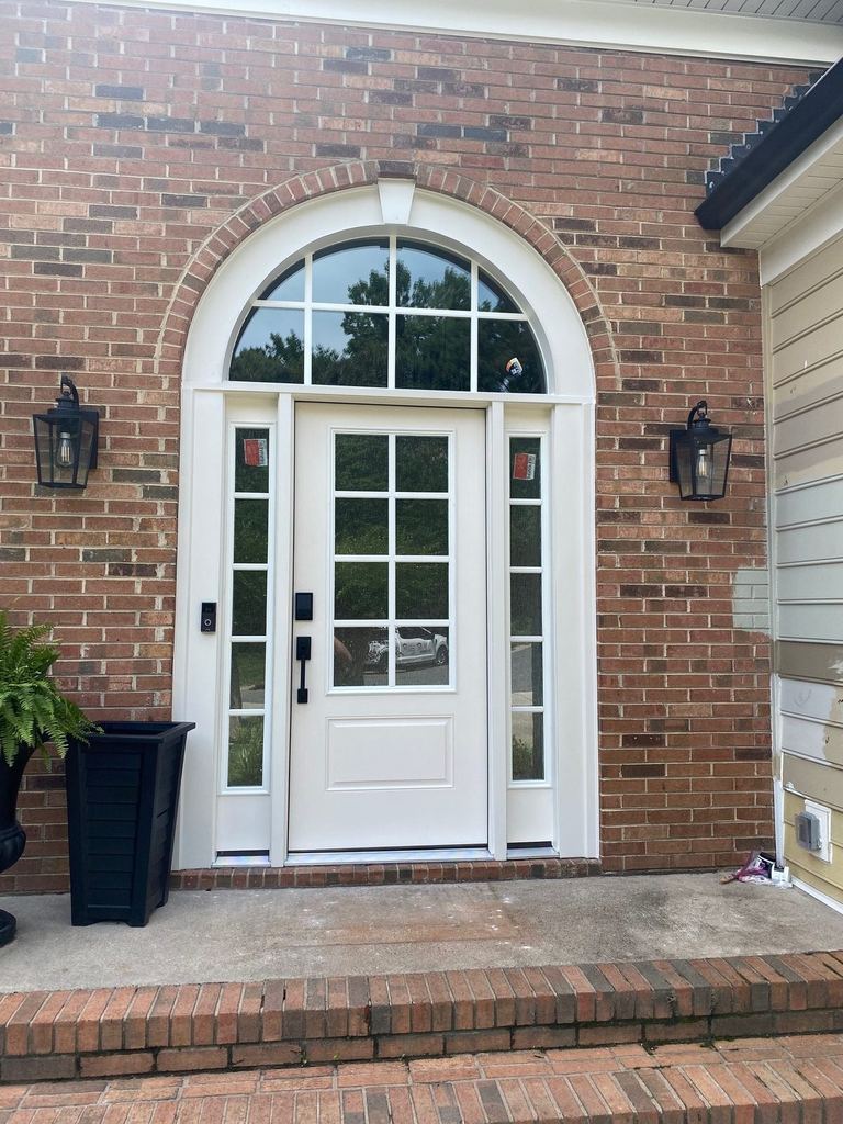A white entry door with sidelights under an arched transom, set into brick, with a wall lantern on each side.