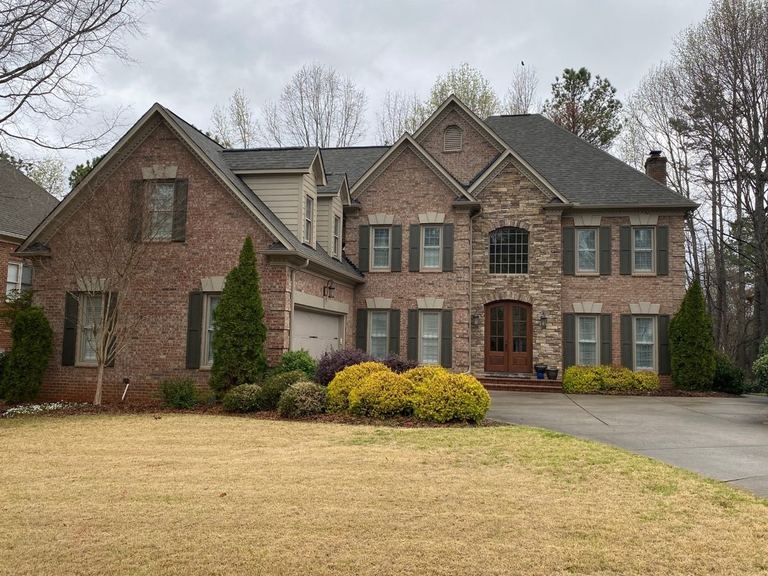 A large brick and stone two-story home in Matthews with a three-car garage and a steep shingle roof, photographed from the street.