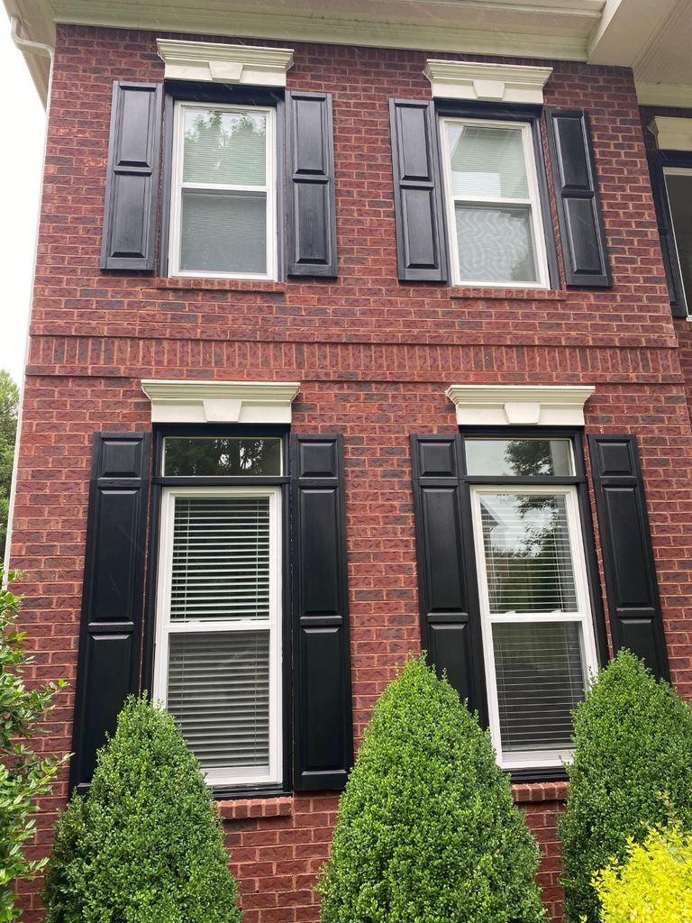 White double-hung replacement windows with black shutters on a red brick home
