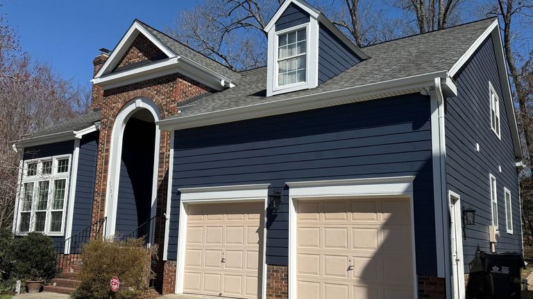 Blue-gray lap siding and white trim above tan garage doors on a Waxhaw home