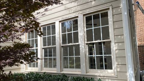 Tall white replacement windows with colonial grilles on a light-sided home