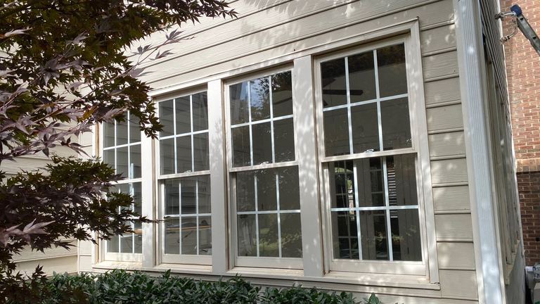 Tall white replacement windows with colonial grilles on a light-sided home