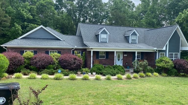 Single-story brick home with a gray shingle roof and landscaped front yard