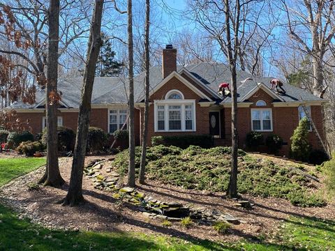 Brick home with a steep shingle roof set among mature trees