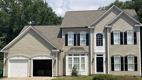 Two-story home in tan lap siding with black shutters and a white garage door
