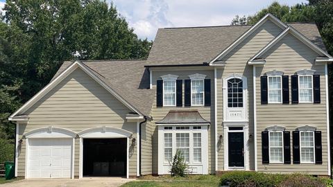 Tan-sided two-story home with black shutters and an attached garage