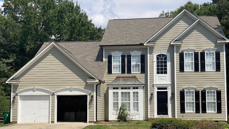 Tan-sided two-story home with black shutters and an attached garage