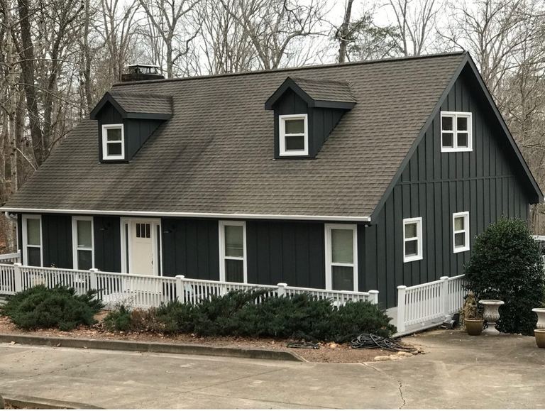 A gambrel-roofed home in Iron Gray board-and-batten HardiePlank with white window trim, three dormers and a white porch rail.